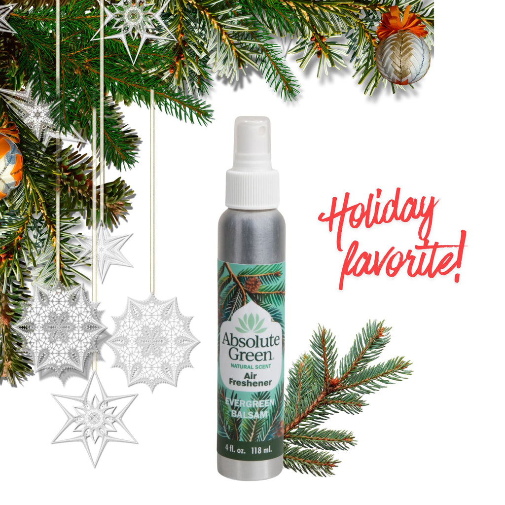 A bottle of Absolute Green Air Freshener centered on a white background, surrounded by holiday decorations including pine branches, ornaments, hanging silver snowflakes, and red script text reading 'Holiday favorite!'.